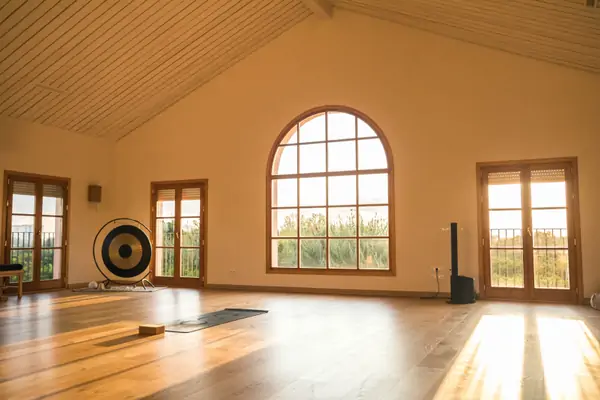 Yoga studio with wooden floors, mats arranged in rows, and large windows allowing natural light to enter.