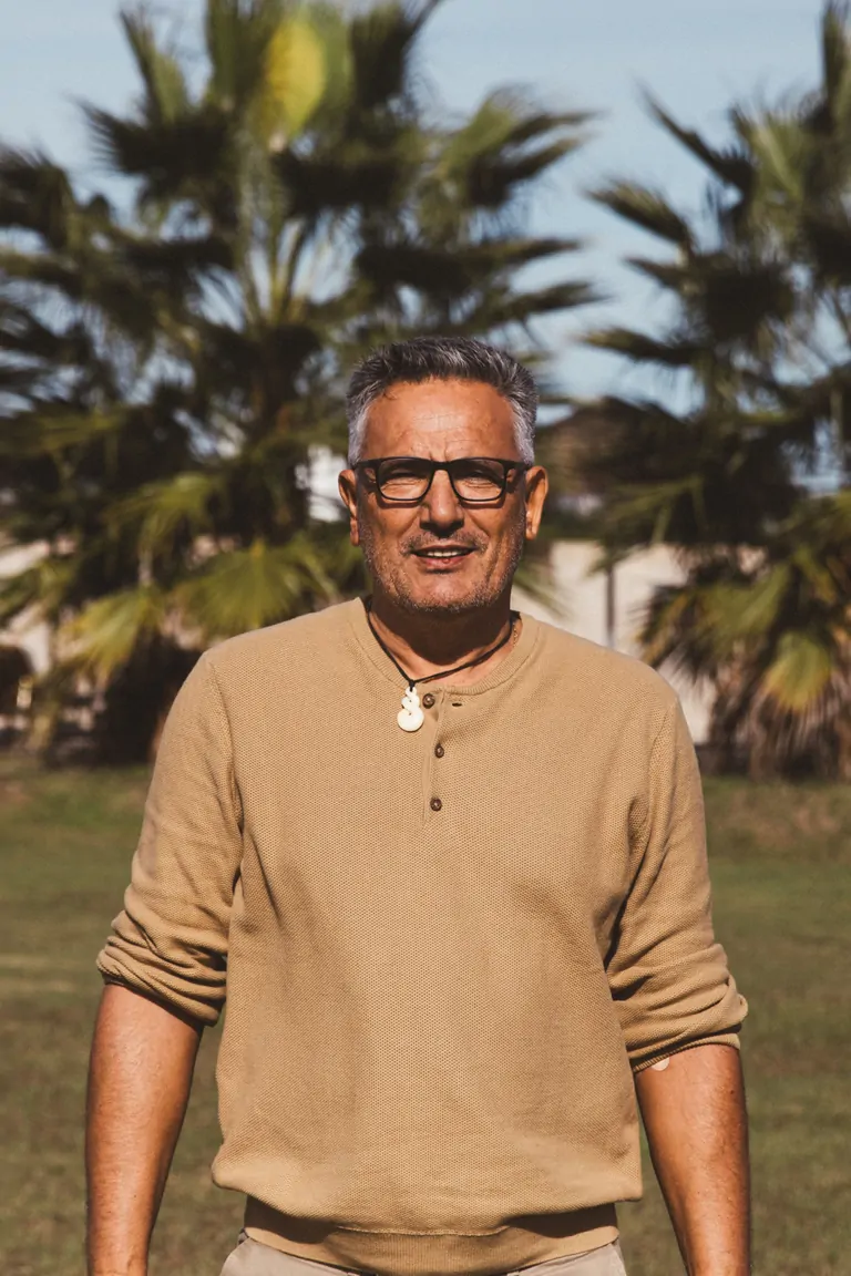 Jean-Paul, Co-founder of Suniai Oliva, stands outdoors, surrounded by lush palm trees under a clear sky.