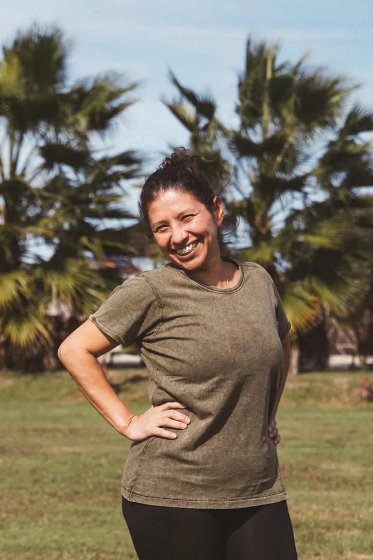 Patty, the space keeper at Suniai Oliva, smiles surrounded by palm trees.