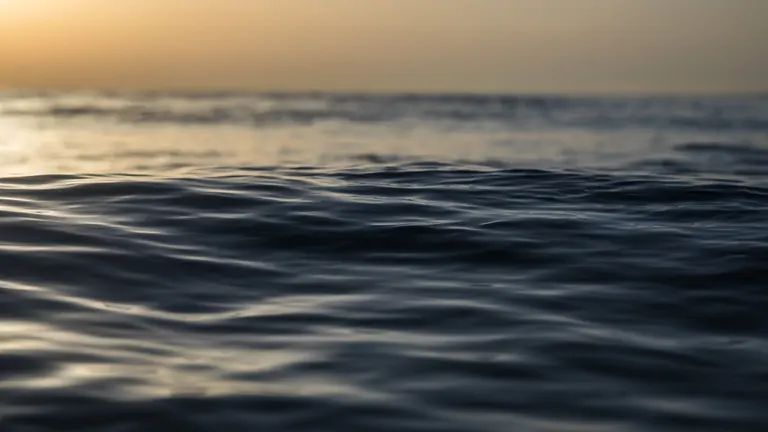 Gentle waves lap the shore at Suniai Oliva Retreat Center by the sea in Spain, with a serene sunset in the background.