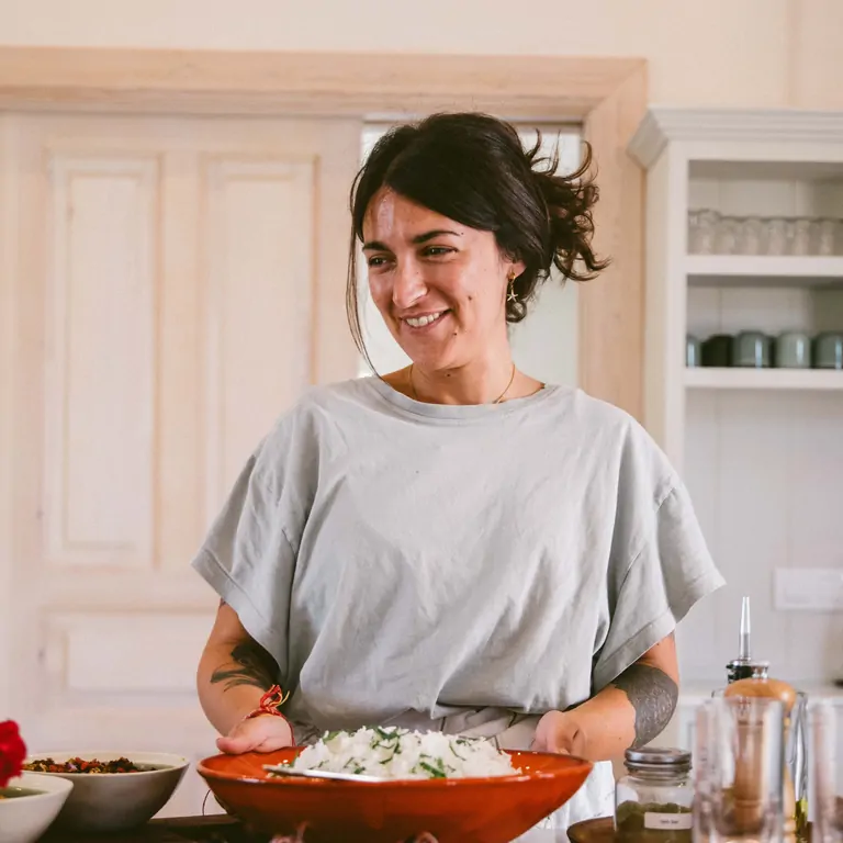 Natalia smiles as she presents a vibrant dish, showcasing her culinary skills in Suniai Oliva's kitchen setting.