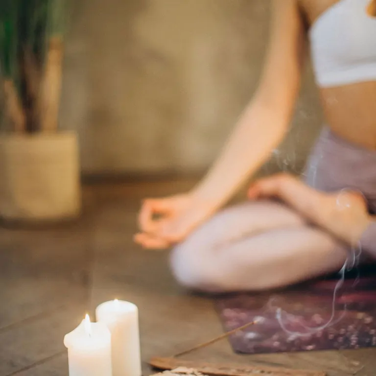 A person meditating in a serene setting with candles and incense on a wooden surface, promoting relaxation and mindfulness.
