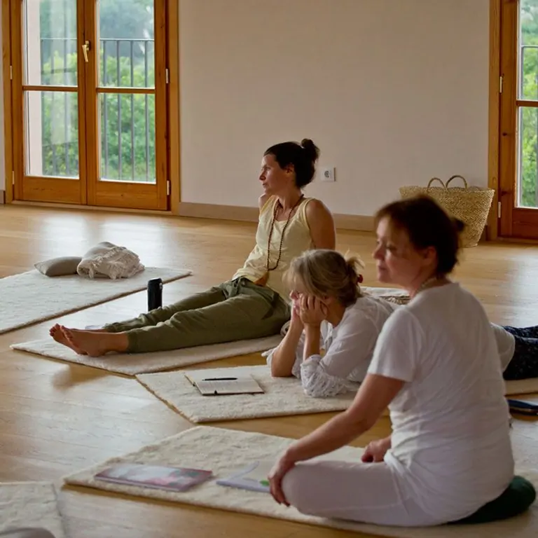 Group of women sitting on mats in a serene yoga studio, engaged in meditation or mindfulness practice. Natural light filters in.