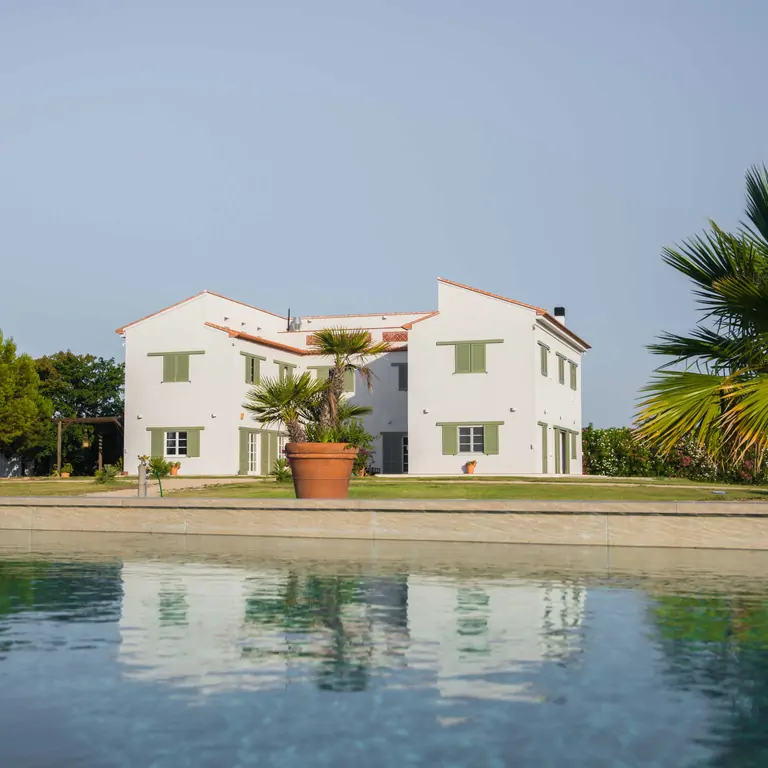 A serene view of Suniai Oliva Retreat Center, featuring a modern building with palm trees beside a reflecting pool.