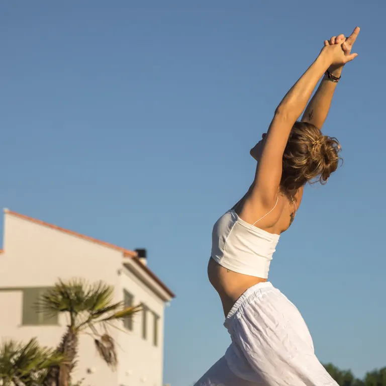A woman stretches joyfully against a clear sky, embodying tranquility at Suniai Oliva Retreat Center.
